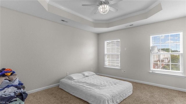 carpeted bedroom featuring ceiling fan, a raised ceiling, ornamental molding, and multiple windows