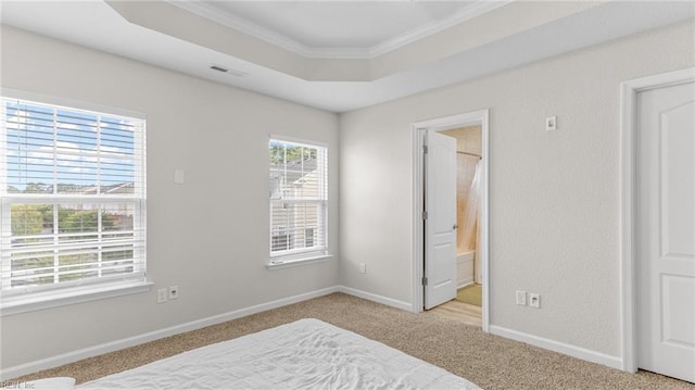 carpeted bedroom with a raised ceiling, connected bathroom, and ornamental molding