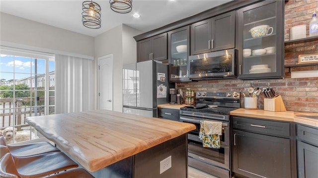 kitchen with wood counters, a kitchen breakfast bar, hanging light fixtures, a kitchen island, and stainless steel appliances