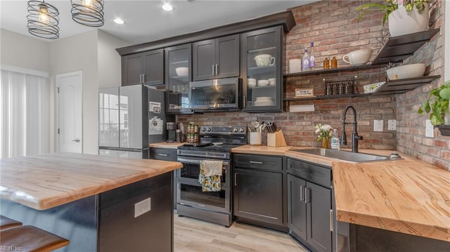 kitchen with sink, butcher block countertops, decorative light fixtures, appliances with stainless steel finishes, and light wood-type flooring