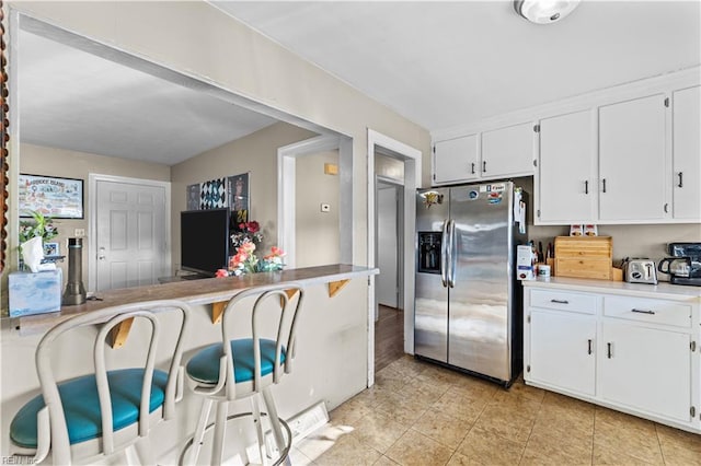 kitchen with kitchen peninsula, stainless steel refrigerator with ice dispenser, a breakfast bar, and white cabinetry