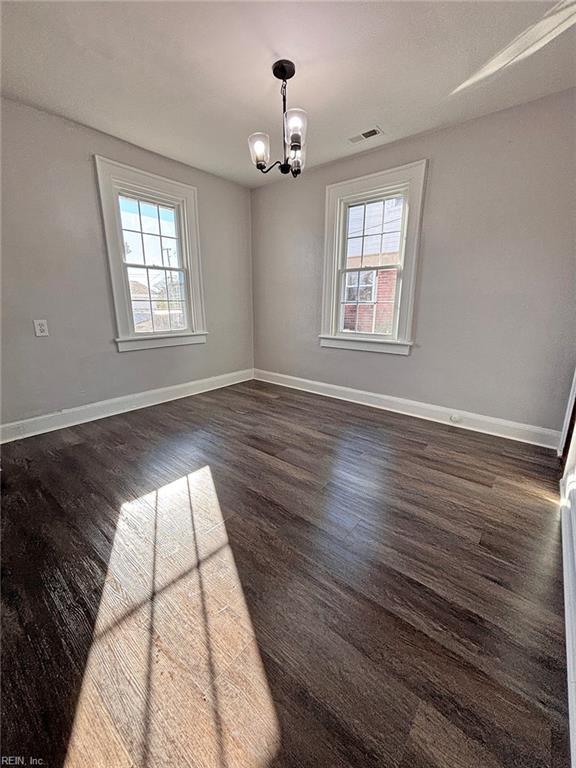 spare room with plenty of natural light, a chandelier, and dark hardwood / wood-style floors