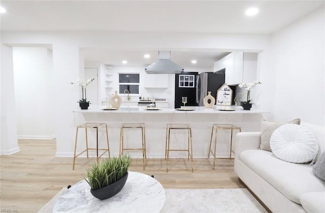 kitchen with white cabinets, stainless steel fridge, a breakfast bar area, and exhaust hood