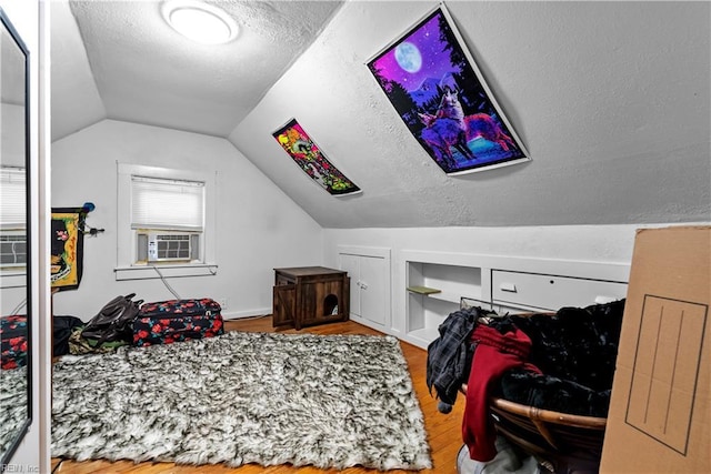 bedroom with hardwood / wood-style floors, cooling unit, a textured ceiling, and vaulted ceiling