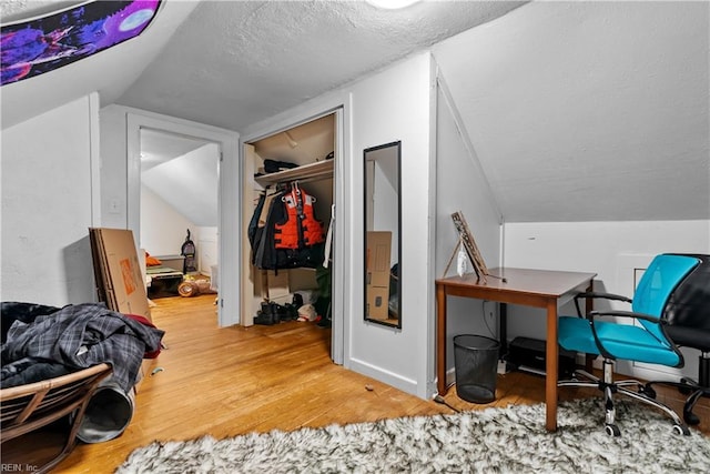 interior space with a textured ceiling, wood-type flooring, and vaulted ceiling