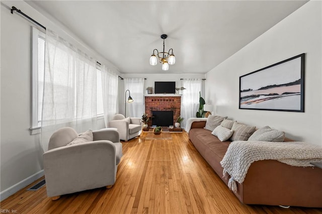 living room featuring a brick fireplace, light hardwood / wood-style flooring, and a notable chandelier