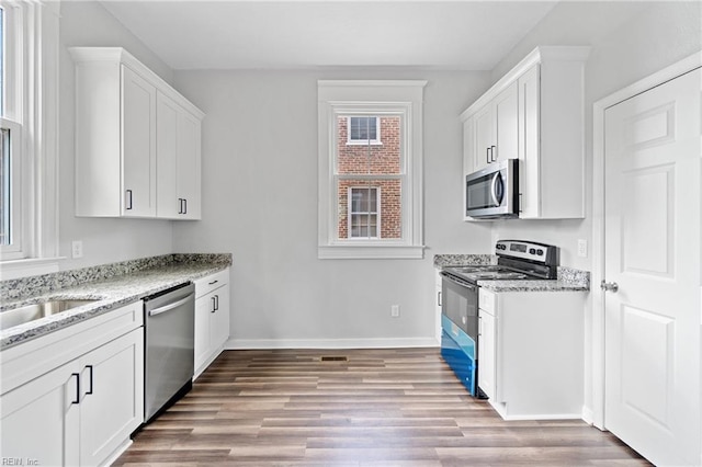 kitchen with white cabinets, light wood-type flooring, light stone countertops, and stainless steel appliances