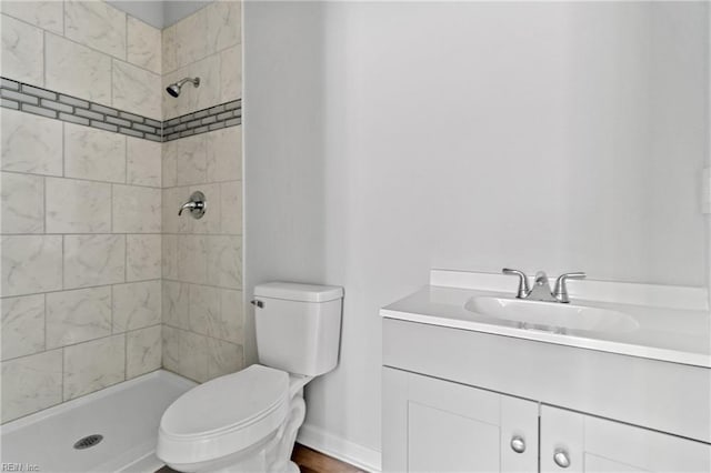 bathroom featuring a tile shower, vanity, and toilet