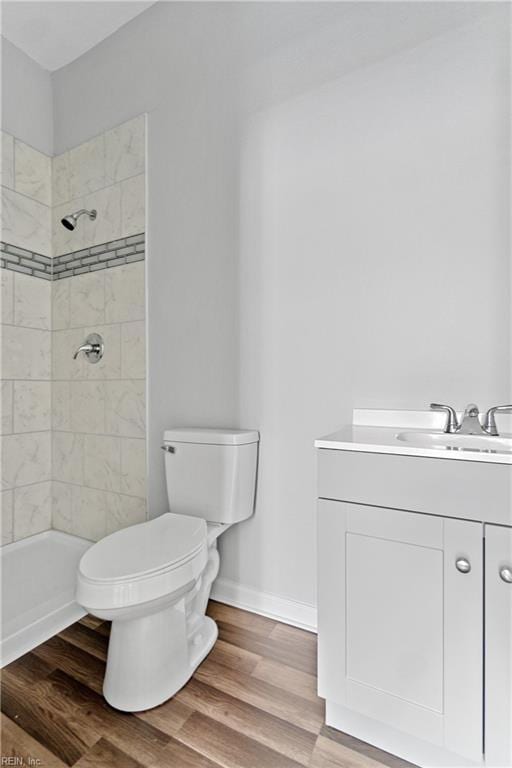 bathroom featuring a tile shower, hardwood / wood-style floors, vanity, and toilet