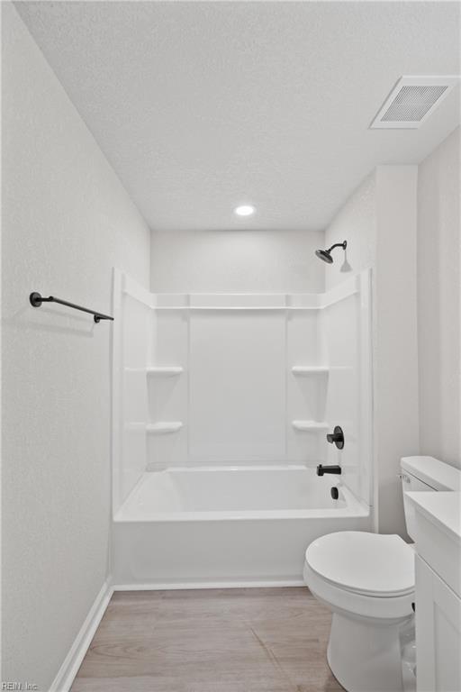 full bathroom featuring tub / shower combination, a textured ceiling, vanity, hardwood / wood-style flooring, and toilet