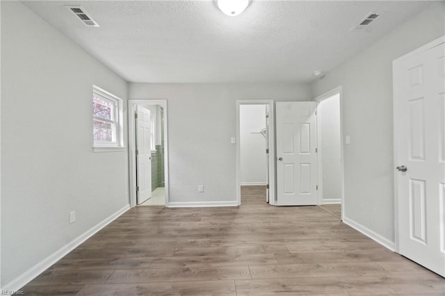 unfurnished bedroom featuring a walk in closet, a closet, light hardwood / wood-style flooring, and ensuite bath