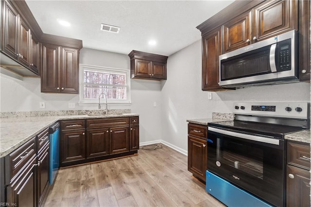 kitchen with light stone countertops, appliances with stainless steel finishes, light wood-type flooring, dark brown cabinets, and sink