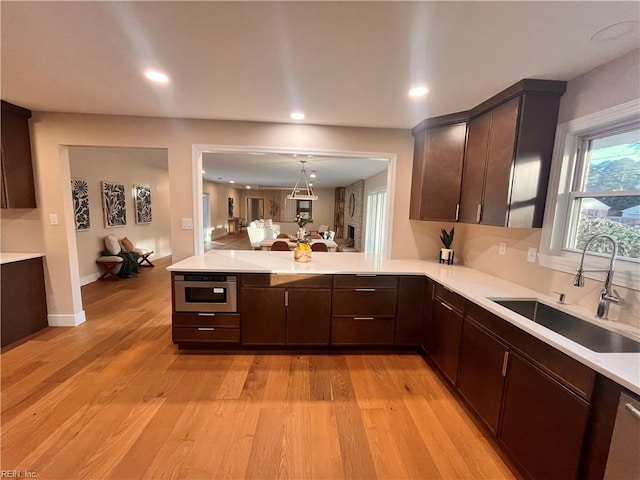 kitchen with hanging light fixtures, sink, dark brown cabinetry, and light hardwood / wood-style flooring