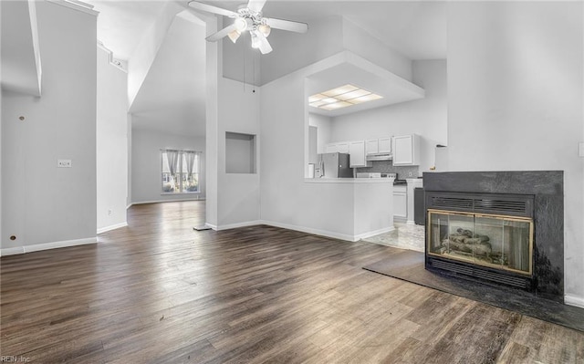 unfurnished living room with ceiling fan, a multi sided fireplace, a towering ceiling, and dark wood-type flooring