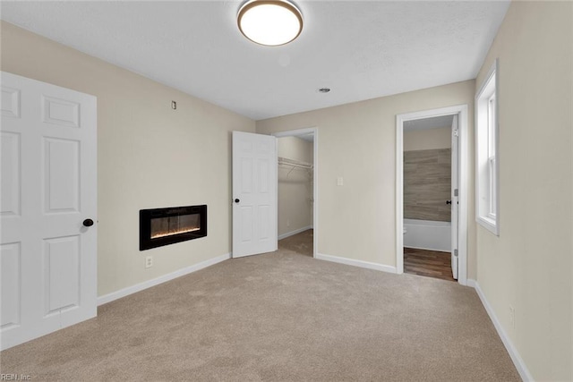 unfurnished bedroom with heating unit, a spacious closet, a closet, and light colored carpet