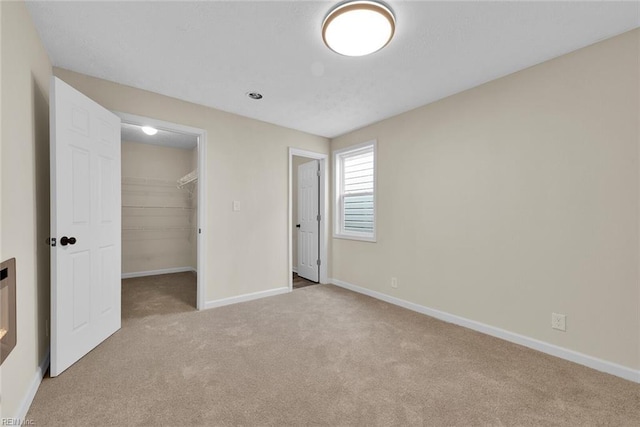 unfurnished bedroom with a walk in closet, light colored carpet, and a closet