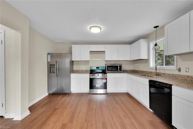 kitchen with appliances with stainless steel finishes, light wood-type flooring, sink, pendant lighting, and white cabinetry