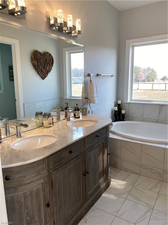 bathroom with a relaxing tiled tub, a wealth of natural light, vanity, and tile patterned flooring