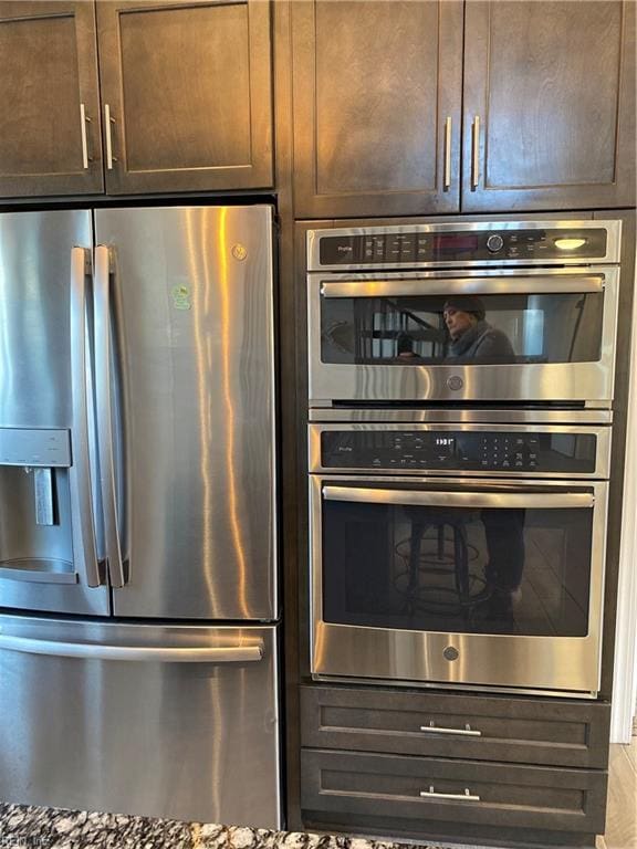 kitchen with stone counters, appliances with stainless steel finishes, and dark brown cabinets