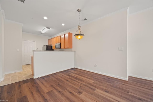 kitchen featuring hanging light fixtures, wood-type flooring, fridge, and crown molding