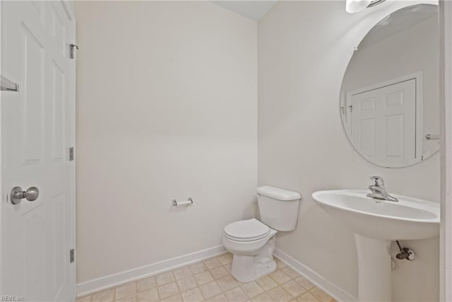 half bath with a sink, tile patterned floors, toilet, and baseboards