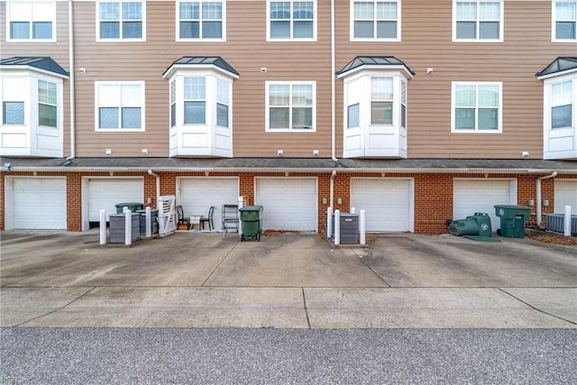 exterior space featuring an attached garage, driveway, central air condition unit, and brick siding