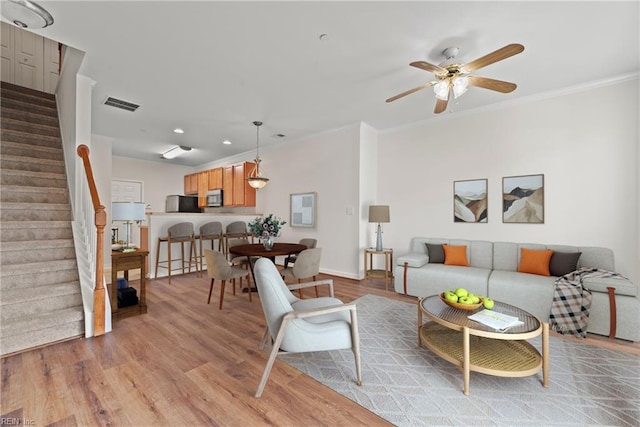 living room featuring light wood-style floors, stairs, visible vents, and a ceiling fan