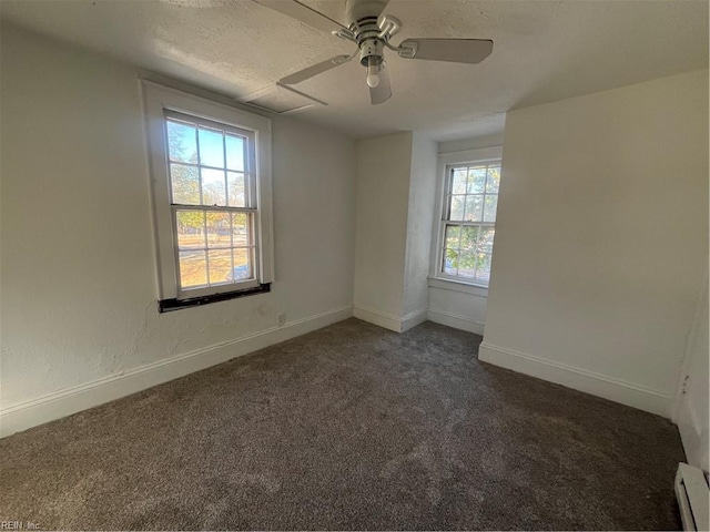 unfurnished room with dark colored carpet, ceiling fan, baseboard heating, and a wealth of natural light