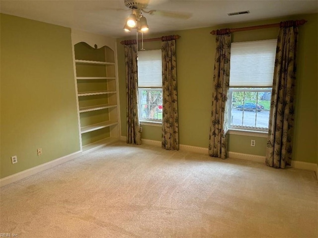 carpeted empty room with built in features, plenty of natural light, and ceiling fan