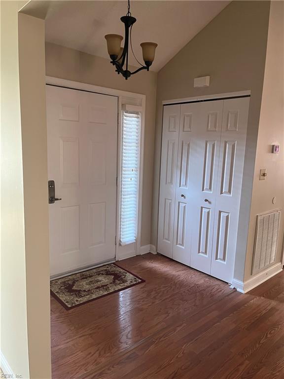 entrance foyer featuring dark hardwood / wood-style flooring, vaulted ceiling, and an inviting chandelier