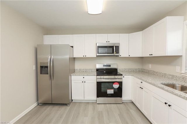 kitchen with light stone countertops, white cabinets, stainless steel appliances, and light hardwood / wood-style floors