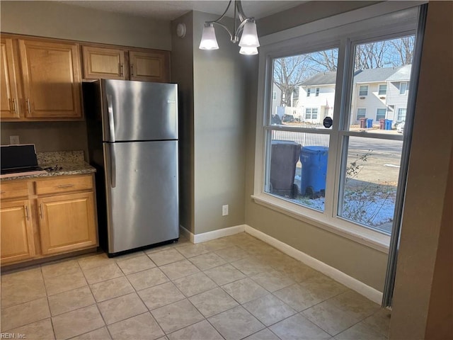 kitchen featuring decorative light fixtures, stainless steel fridge, light stone countertops, a wealth of natural light, and a notable chandelier