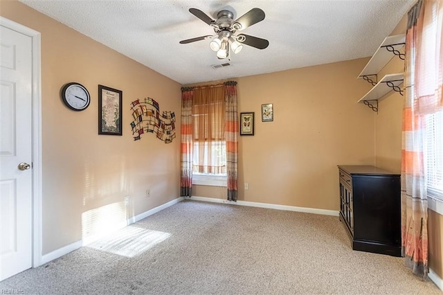 interior space with a textured ceiling, light colored carpet, and ceiling fan