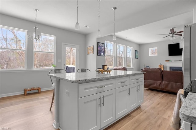 kitchen with white cabinetry, hanging light fixtures, light stone countertops, a breakfast bar area, and ceiling fan with notable chandelier