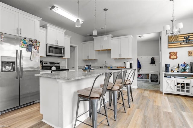 kitchen with white cabinets, a kitchen island, stainless steel appliances, hanging light fixtures, and a breakfast bar area