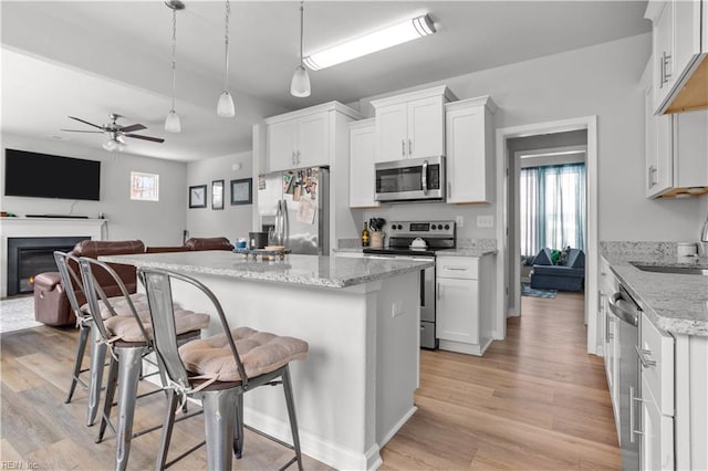 kitchen with light stone counters, appliances with stainless steel finishes, white cabinetry, and hanging light fixtures