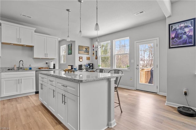 kitchen featuring light stone counters, a kitchen island, white cabinetry, and hanging light fixtures