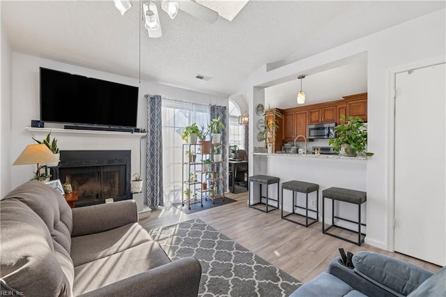 living room featuring ceiling fan, light hardwood / wood-style floors, a textured ceiling, and vaulted ceiling