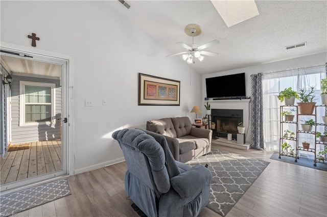 living room featuring ceiling fan, light wood-type flooring, lofted ceiling with skylight, and a textured ceiling