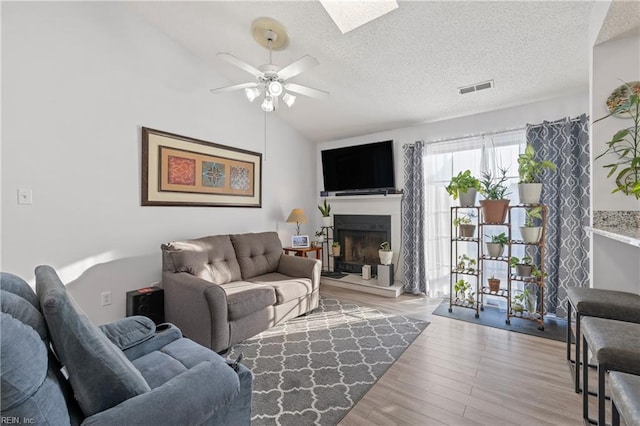 living room featuring lofted ceiling, ceiling fan, light hardwood / wood-style floors, and a textured ceiling