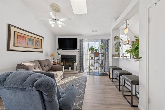 living room with a textured ceiling, ceiling fan, light hardwood / wood-style flooring, and lofted ceiling