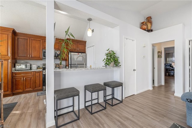 kitchen featuring a breakfast bar, vaulted ceiling, stainless steel appliances, and light stone counters