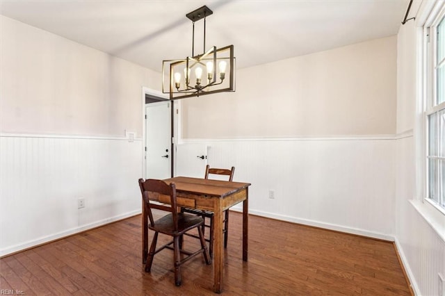 dining area with dark wood-type flooring and an inviting chandelier