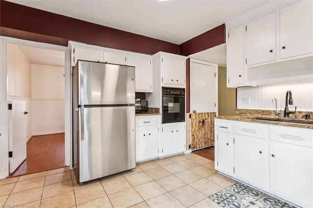 kitchen with black oven, white cabinetry, and stainless steel refrigerator