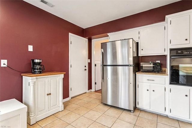 kitchen featuring light tile patterned flooring, stainless steel refrigerator, oven, and white cabinetry