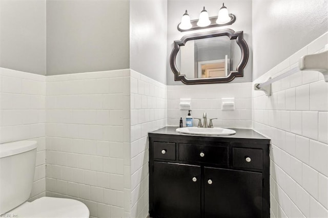 bathroom featuring toilet, vanity, and tile walls