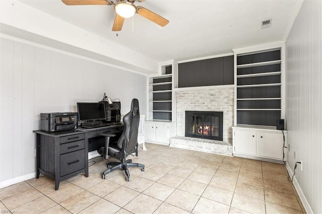 home office with a brick fireplace, light tile patterned flooring, ceiling fan, and built in shelves