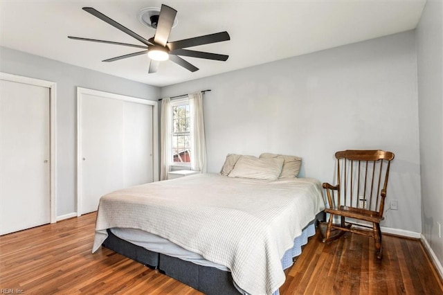 bedroom with ceiling fan, dark hardwood / wood-style floors, and multiple closets