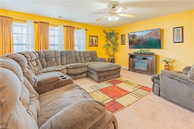 living room with light colored carpet, visible vents, a glass covered fireplace, ceiling fan, and baseboards