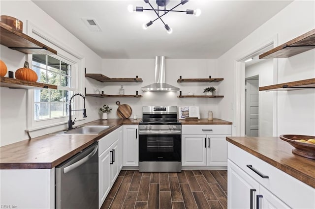 kitchen with white cabinets, stainless steel appliances, wall chimney exhaust hood, sink, and butcher block counters